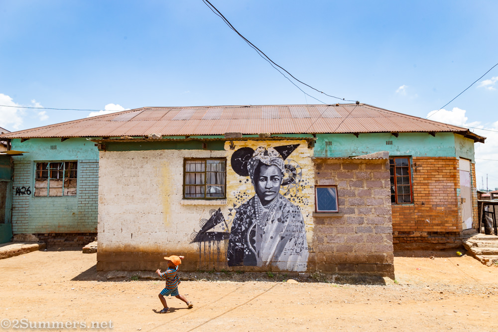 Child in Kliptown, Soweto, running past a mural of Charlotte Maxeke